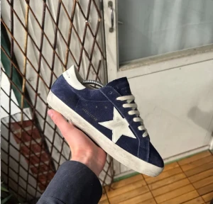 Blåa sneakers från Golden Goose - Snygga blåa sneakers från Golden Goose med vit stjärndetalj på sidan och vita skosnören. Ovandelen är i mocka och sulan är vit med en något sliten look. Klassisk låg modell som passar till många stilar.