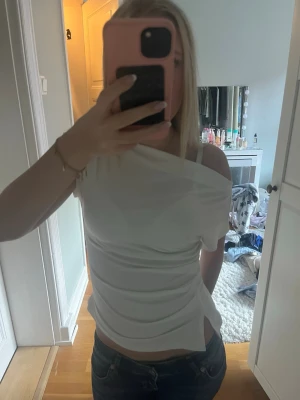 Vit oneshoulder topp - Snygg vit oneshoulder topp med draperad effekt och tight passform. Perfekt för dig som vill ha en trendig och stilren look. Toppen är ärmlös och har en asymmetrisk axel som ger en unik touch.