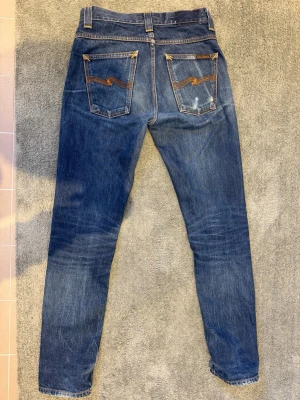 Nudie Jeans Grim Tim Dry Ring - Säljer ett par Nudie jeans i w28 l32 modell grim Tim färg dry ring. De har en slim passform med bra fades. Patchen där bak är borta och de har ytterst lite slitna i grenen (se bild).