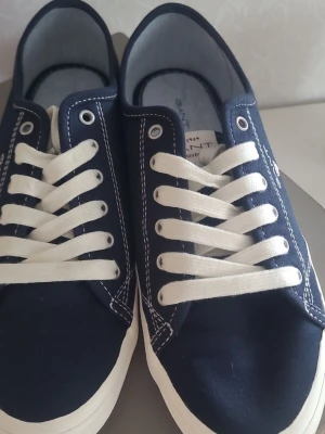 Gant Preptown sneakers i marinblå, storlek 38 - Gant Preptown sneakers i marinblå med vita snören och vita sulor. Skorna har en klassisk design med snörning och Gant-logotypen synlig på sidan och bak på sulan. Innersulan är också märkt med Gant. Skorna är I toppskick