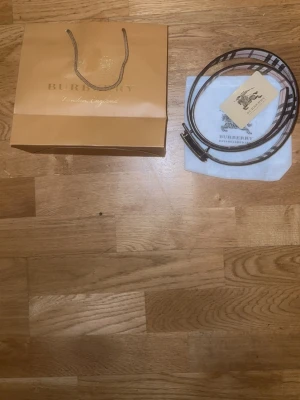  rutigt bälte i skinn - Säljer ett klassiskt bälte med ikoniskt rutigt mönster i beige, svart och vitt. Bältet är tillverkat i skinn och har en elegant metallspänne. Perfekt för att lyfta din outfit med en lyxig touch.