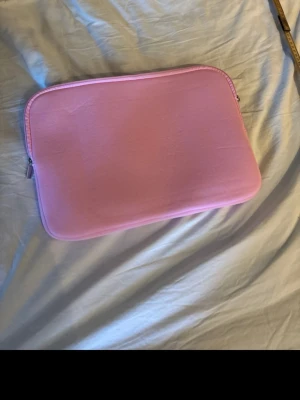Rosa datorväska med dragkedja - En stilren och enkel rosa datorväska i mjukt material. Väskan har en slät yta och stängs med dragkedja. Perfekt för att skydda din laptop och lätt att bära med sig. Passar dig som gillar färg och vill ha något som sticker ut. Endast testad men aldrig använd. 