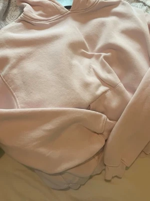 Ljusrosa hoodie med huva - Mysig ljusrosa hoodie med klassisk huva och stor magficka framtill. Tillverkad i mjukt sweatshirtmaterial som känns skönt mot huden. Perfekt för chill dagar eller när du vill ha en enkel och stilren look. 💛