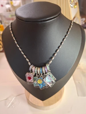 Halsband med färgglada berlocker - Unikt halsband med silverfärgad kedja och flera rektangulära berlocker i olika färger och motiv, bland annat hjärta, sol och måne. Berlockerna har detaljer i rött, gult, blått och lila samt skimrande ringar. Perfekt för dig som gillar färgstarka accessoarer.