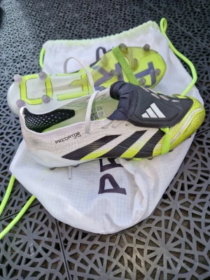 Adidas Predator fotbollsskor svart/vit - Säljer ett par Adidas Predator fotbollsskor i svart, vitt och neongult. Skorna har klassisk låg profil, snörning och gummidobbar för bra grepp på planen. Tillverkade i syntetmaterial med tydliga Predator-detaljer och medföljande vit dragskopåse. Använda 1 månad. AG dubb. Elite