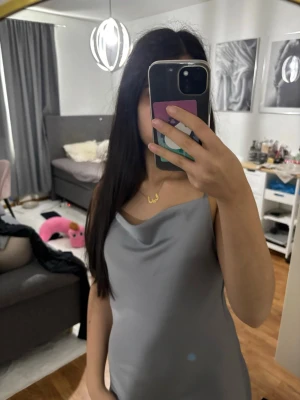 Grå långklänning med slätt tyg - Snygg grå långklänning med slätt och elegant tyg. Klänningen har en enkel och stilren design med smala axelband och en mjuk drapering vid halsen. Perfekt för dig som gillar minimalistisk stil och vill ha något som känns både trendigt och klassiskt.