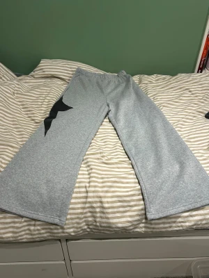Grå mjukisbyxor med svart stjärna - Säljer ett par grå mjukisbyxor med breda ben och elastisk midja. På vänster ben finns en stor svart stjärndetalj, bara på framsidan💕 Storlek S