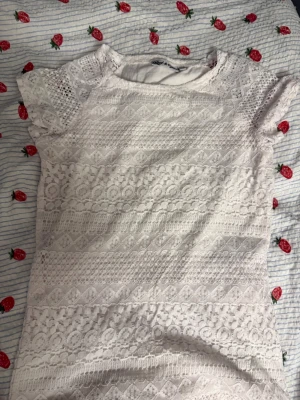 Vit spetsklänning från Red & Blue - Säljer en vit kortklänning från Red & Blue med vacker spets och korta ärmar. Klänningen har ett detaljerat spetsmönster och rund halsringning. Perfekt för dig som gillar romantiska och feminina plagg.