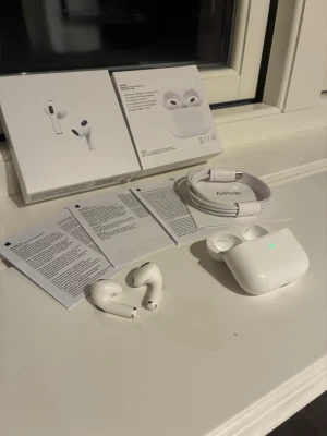 Apple AirPods 3 med laddningsetui - Säljer ett par vita Apple AirPods 3 med tillhörande laddningsetui och USB-C kabel. Hörlurarna har en stilren och kompakt design i blankt plastmaterial. Perfekt för dig som vill ha trådlösa hörlurar med bra ljud och enkel anslutning till Apple-enheter.