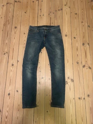 Blå Nudie Jeans - Säljer ett par blå slim fit jeans från Nudie Jeans. Jeansen har normal midja, dragkedjegylf och är tillverkade i denim med lite stretch för extra komfort. Storlek w27 l27/28. Säljer för att de är för små för mig. Skriv gärna till mig vid funderingar!