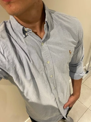 Ljusblå skjorta från Polo Ralph Lauren - Säljer en klassisk ljusblå skjorta från Polo Ralph Lauren med button-down krage och broderad logga på bröstet. Skjortan har långa ärmar och vita knappar framtill. Perfekt för dig som gillar stilrena plagg med ikonisk design.💋modellen bör storlek M, den har ingen knapp i kragen men har sytt så det spelar ingen roll💋