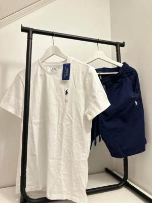 Marinblå shorts Polo Ralph Lauren - Snygga marinblå shorts Polo Ralph Lauren med klassisk logga broderad på benet. Shorts med elastisk midja och snörning för skön passform. Perfekta för sommaren och har en stilren look som passar till många outfits.