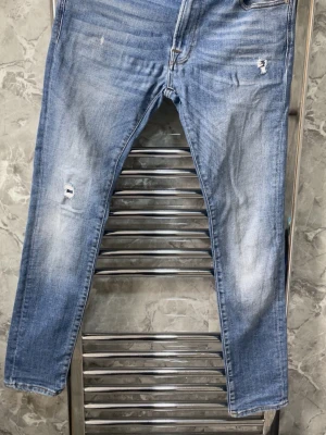 Ljusblå slitna skinny jeans - Säljer ett par ljusblå skinny jeans med slitningar och hål på låret och knät. Jeansen har klassisk femficksdesign och lätt tvättad look med blekta partier. Perfekta för en avslappnad streetstil.