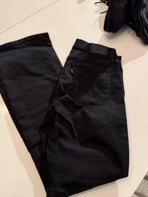 Svarta jeans från Levi's - Säljer ett par klassiska svarta jeans från Levi's med raka ben och femficksdesign. Jeansen har en snygg svart Levi's-label på bakfickan och är tillverkade i bomull. Perfekta för dig som vill ha en tidlös och cool look.