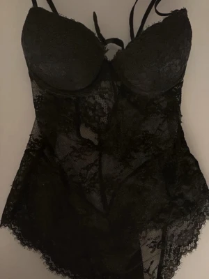 Svart spetsbody med blommönster - Säljer en svart body i transparent spets med blommönster. 75A XS