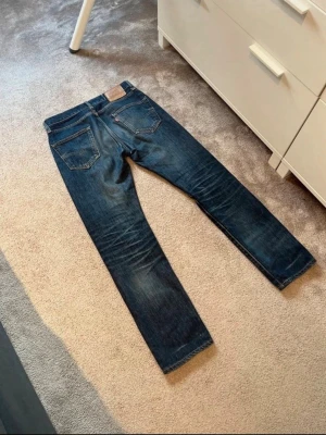 Mörkblå jeans från Levi's - Snygga mörkblå jeans från Levi's med klassisk femficksdesign och raka ben. Jeansen har subtila slitningar och en ikonisk läderpatch baktill i midjan. Perfekta för en avslappnad och trendig look.