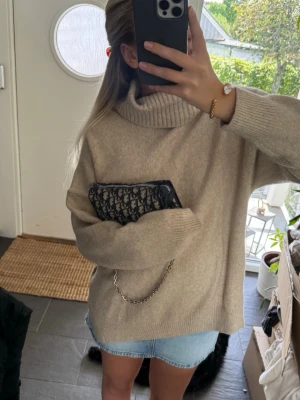 Beige polotröja i mjuk ullmix - Säljer en oversized beige polotröja med bred ribbad krage och långa ärmar. Tröjan är stickad i en mjuk ullmix och har en avslappnad passform som passar perfekt till jeans eller kjol. Enkel och stilren design som är lätt att matcha.