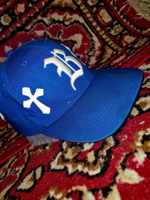 Chrome hearts Blå keps med broderade kors - Snygg blå keps med böjd skärm och broderade vita kors samt bokstäver framtill. På baksidan står det 'Live or Die' i vit text. Kepsen har klassisk passform och är tillverkad i bomullstyg.