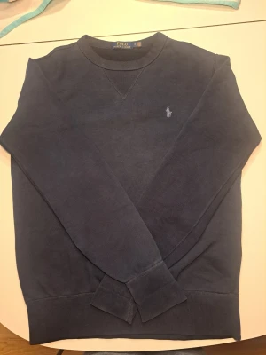 Polo Ralph Lauren tröj - Mörkblå sweatshirt från Polo Ralph Lauren med rund halsringning och broderad logga på bröstet. Tröjan har ribbade muddar vid ärmslut och nederkant samt klassisk college-look. Perfekt för en avslappnad och stilren outfit.                                                                Mått: Byst ca 56 cm, armhåla ner ca 47cm, midja bredd ca 47 cm (instretchad), axel till armslut 68 cm, bak ner ca 70 cm                          Pris diskuteras gärna i DM!!