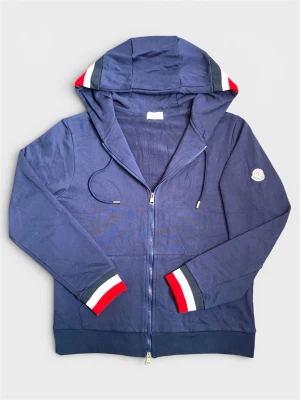 Marinblå hoodie från Moncler - Snygg marinblå hoodie från Moncler med dragkedja, huva och dragsko. Ärmsluten och huvan har detaljer i rött, vitt och blått. Moncler-logga på vänster ärm. Tillverkad i mjukt bomullsmaterial för en bekväm känsla.