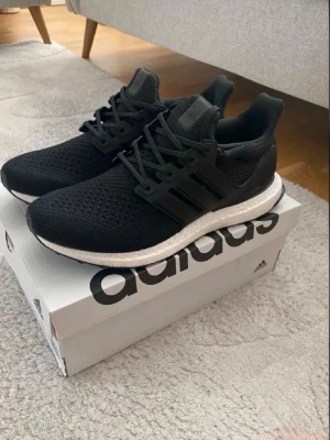 Adidas Ultra Boost svarta vitt - Svarta Adidas Ultra Boost sneakers med stickad ovandel och klassiska tre ränder på sidan. Skorna har en vit Boost-sula för extra komfort och svart yttersula. Perfekta för dig som gillar sportig och stilren look.