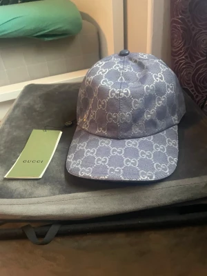 Blå keps från Gucci med GG-mönster - Snygg blå keps från Gucci med det klassiska GG-monogrammet över hela kepsen. Kepsen har böjd skärm och justerbar baksida. Tillverkad i canvasmaterial med exklusiv känsla. Perfekt accessoar för att lyfta din outfit.