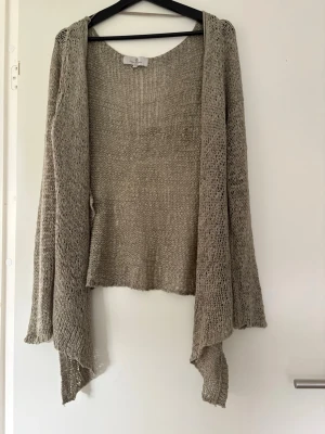 Beige stickad kofta från Flash Woman - Säljer en beige stickad kofta från Flash Woman. Koftan har öppen front, lång ärm och ett tunt, luftigt material med avslappnad passform och asymmetrisk nederkant. Perfekt för lager på lager och enkel att matcha till olika outfits.