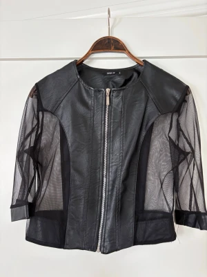 Svart skinnjacka med meshdetaljer - Cool svart skinnjacka från Nuna Lie med unika meshärmar och dragkedja framtill. Jackan har en modern, kortare passform och stilrena detaljer som ger en edgy look. Köpt i Italien! Storlek S och aldrig använd 