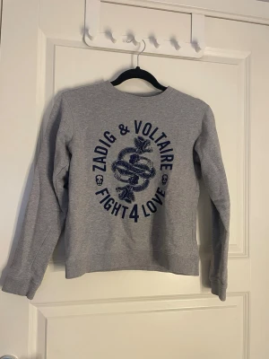 Grå sweatshirt Zadig & Voltaire - Grå sweatshirt från Zadig & Voltaire med tryck i mörkblått. Det står ingen storlek i tröjan men jag skulle säga att den är 146/152, xxs. Säljer då den tyvärr är för liten för mig. Endast använd fåtal gånger.