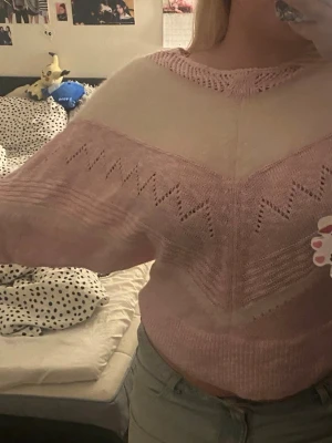 Ljusrosa och vit stickad tröja - Superfin stickad tröja i ljusrosa och vitt med snyggt sicksackmönster och håldetaljer över bröstet och ärmarna. Tröjan har en lös passform och rund halsringning. Perfekt för dig som gillar mjuka pasteller och mysiga plagg.