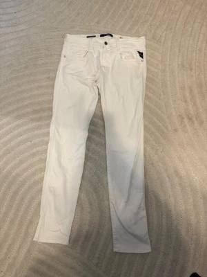 Vita Replay Hyperflex jeans - Snygga vita jeans från Replay Hyperflex med klassisk femficksdesign och raka ben. Jeansen har en diskret logga på bakfickan och är tillverkade i ett stretchigt material som ger skön passform. Perfekta för dig som gillar stilrena och fräscha jeans.