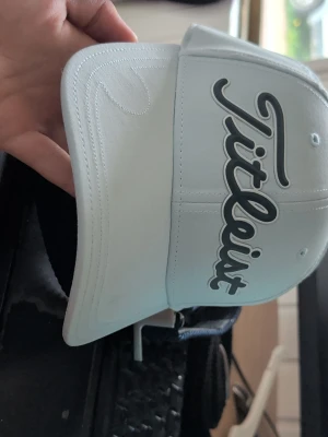 Ljusblå Titleist keps med brodyr - Snygg ljusblå keps från Titleist med stor broderad logga framtill. Justerbar baktill för perfekt passform. Kepsen är tillverkad i ett lätt och bekvämt material, perfekt för golf eller vardagsstil.