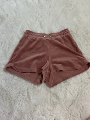 Rosa velourshorts från Gina Tricot - Mysiga rosa shorts i mjuk velour från Gina Tricot. De har elastisk midja, två knappar framtill och en avslappnad passform. Perfekta för varma dagar eller chill hemma. Supersköna och trendiga!