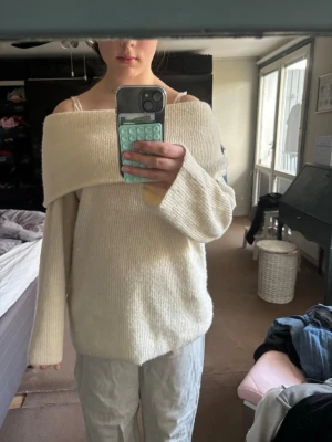 Off shoulder stickad tröja i cremevitt - Säljer en oversized stickad tröja i cremevitt med off shoulder-modell och bred krage. Tröjan har långa ärmar och är gjord i ett mjukt, ribbstickat material. Perfekt för en chill och trendig look.