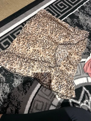 Leopardmönstrad omlottkjol med volang - Snygg kort omlottkjol med leopardmönster i beige och bruna toner. Kjolen har en volang längs nederkanten som ger en trendig och lekfull look. Perfekt för dig som vill sticka ut med ett djurmönster. Materialet känns lätt och luftigt.