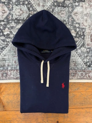 Mörkblå Polo Ralph Lauren Hoodie - Storlek XS - Tjena, säljer en riktigt snygg, marinblå Hoodie från Polo Ralph Lauren. Hoodien är i sig i mycket gott skick och är helt fläckfri. Däremot har storlekslappen/nackettiketten blivit avklippt av en tidigare ägare. Storlek XS. Tröjan är jättefräsch, och passar till i princip allt. Fraktar snabbt!✅📦🚛Hör av er vid frågor!😁💯