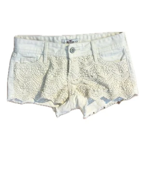 Vita spetsdetaljerade shorts Hollister - Snygga vita shorts från Hollister med spetsdetaljer framtill och råa kanter. Klassisk femficksmodell med knapp och dragkedja. Perfekta för varma dagar och ger en fräsch och somrig look.