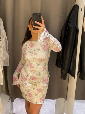 Blommig vit kortklänning med spets  - Supersöt vit kortklänning med blommigt mönster i rosa och blå toner. Klänningen är i spets och en figurnära passform. Perfekt för vår och sommar, och ger en romantisk vibe. Använd 1 gång 