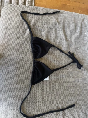 Svart trekantsbikini med knyt - Snygg svart trekantsbikini med knyt i nacken och ryggen. Klassisk modell som är enkel att justera för perfekt passform. Perfekt för stranden eller poolen. Stilren och tidlös design som passar till allt. Fungerar ofta i många olika storlekar 