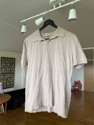 Beige polotopp från H&M - Stilren beige polotopp från H&M med klassisk krage och knäppning framtill. Toppen har korta ärmar och är tillverkad i ett mjukt material som känns skönt mot huden. Perfekt för en avslappnad och trendig look.