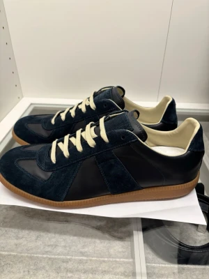 Mörkblå sneakers med mockadetaljer - Snygga mörkblå sneakers med ovandel i både mocka och slätt läder, beige innersida och vita snören. Skorna har en klassisk gummisula i brunt och stilren design som passar till det mesta. Perfekta för dig som gillar en clean och tidlös look.