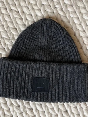 Acne mössa - Säljer en mörkgrå ribbstickad mössa från Acne Studios med den klassiska ansiktsloggan framtill💓💓
