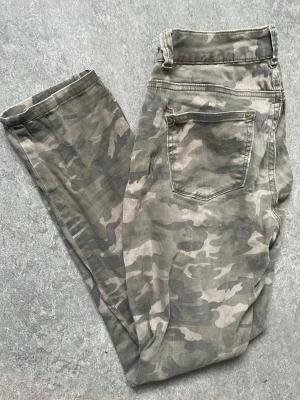 Camo-mönstrade skinny i ”stretch” - Snygga camo-mönstrade skinny jeans i gröna och beige toner. Jeansen har klassisk femficksdesign och normal midja. Perfekta för dig som vill ha en streetwear-inspirerad look. Väl använda men har ett par år till på nacken. Mina absoluta favissar som är för små! 
