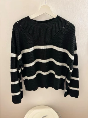 Svart stickad tröja med vita ränder - Säljer en svart stickad tröja med breda vita ränder. Tröjan har rund halsringning, lång ärm och är ribbstickad för extra struktur. Perfekt för dig som gillar en enkel men snygg look.