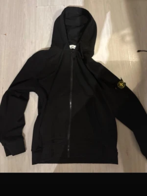 Svart hoodie från Stone Island - Säljer en svart zip tröja  från Stone Island med dragkedja framtill och klassisk logopatch på vänster ärm. Tröjan har huva och två fickor storlek xxl men passsr L inte riktigt 