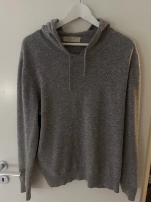 Grå cashmere hoodie från Sayless - Mjuk och stilren grå hoodie från Sayless med huva och dragsko. Tillverkad i ett skönt material som passar perfekt för en avslappnad look. Långärmad modell med ribbade muddar vid ärmslut och nederkant. Storlek M passar mer S