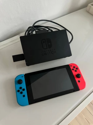 Nintendo Switch  - Nintendo Switch spelkonsol med röd och blå Joy-Con-kontroller. Dockningsstation och kablar ingår. Perfekt för gaming både hemma och på språng.
