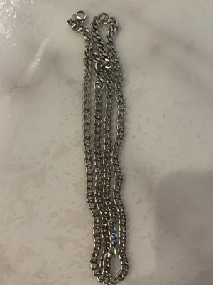 Silverfärgat kedjehalsband - Snyggt halsband i silverfärgad metall med klassisk kedjedesign. Halsbandet har en robust karbinhake och passar perfekt för dig som gillar stilrena accessoarer med lite edge. Perfekt att bära som det är eller att kombinera med andra smycken.