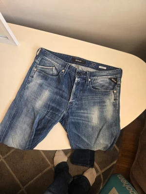 Blå jeans från Replay, storlek w32 L32 - Snygga blå jeans från Replay i klassisk femficksmodell. Jeansen har en tvättad look med slitningar och ljusare partier framtill. Tillverkade i denim med en rak passform och normal midja. Perfekta för en avslappnad och trendig stil.