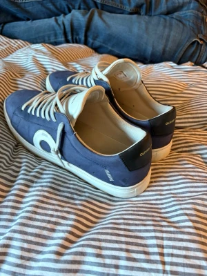  Oliver Cabell  - Snygga blå sneakers från Oliver Cabell med vita detaljer och vita skosnören. Skorna har en låg profil, vit sula och en rundad tå. Materialet ser ut att vara läder eller mocka och de har en cool cirkeldetalj på sidan. Perfekta för en stilren och avslappnad look. Skorna är i topp skick finns nästan inga andra Oliver Cabell skor i det här skicket på Plick i denna modell, priset går att diskuteras vid en snabb och smidig affär.